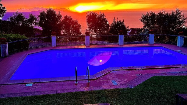 Une piscine avec vue sur le coucher de soleil, entourée de pelouse et agrémentée de quelques chaises longues.
