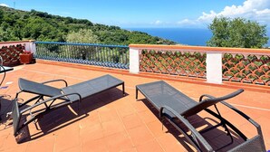 Une terrasse avec deux fauteuils, une table et une vue sur la mer et les collines.