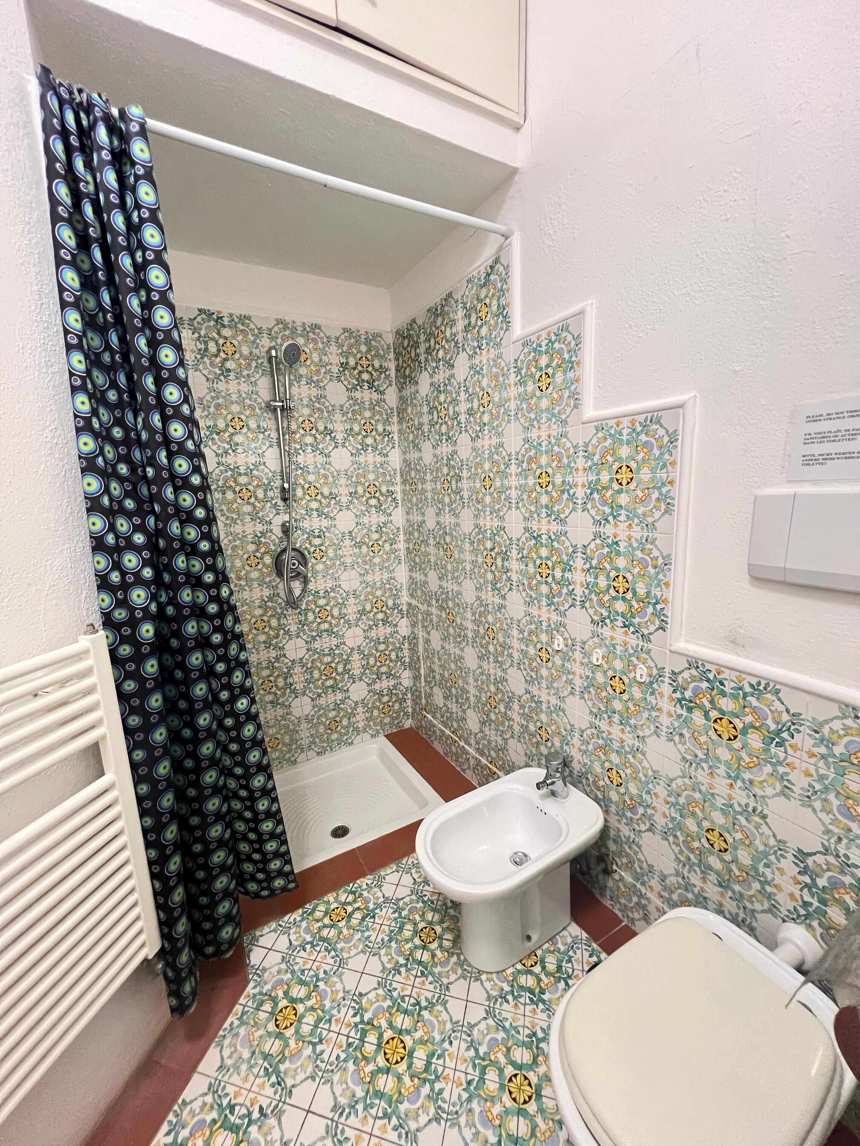 Ein Badezimmer mit Dusche, Bidet und Toilette. Die Wände sind mit einem Blumenmuster gefliest.