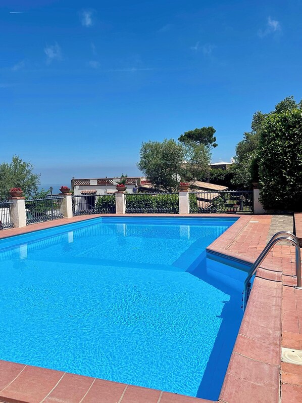 A rectangular swimming pool with clear blue water, surrounded by a brick deck and metal railings.