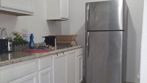 Una cocina con armarios blancos, un refrigerador de acero inoxidable, un lavamanos y una encimera con diversos objetos.
