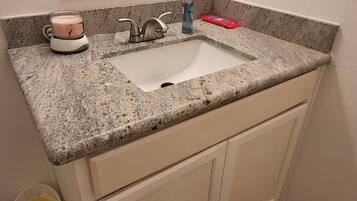 A bathroom with a granite countertop sink, a mirror above it, and a white cabinet below.