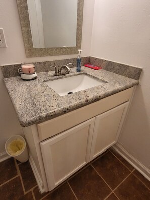 Un bany amb un lavabo de superfície de granit, un mirall a dalt i un armari blanc a sota.