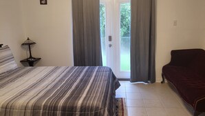 Un dormitorio con cama, mesita de noche, lámpara, sofá de color oscuro y puerta corrediza de vidrio que da a un balcón.