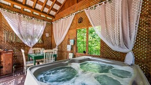 A hot tub in a wooden cabin with a table and chairs, surrounded by curtains and a wooden lattice wall.
