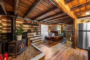 Interior de uma cabana de toras com lareira, paredes de madeira, sofá e geladeira.