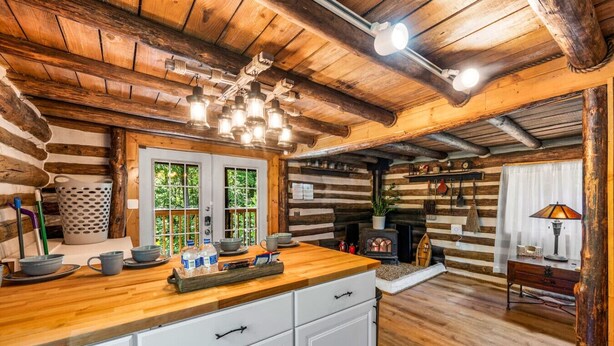 A rustic cabin interior with a wooden dining table, white cabinets, a fireplace, and a hanging light fixture.