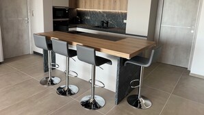 A modern kitchen with a wooden island and bar stools, equipped with a built-in microwave and oven. - Apartment (Viggianello)