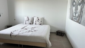 A bedroom with a bed, white bedding, a small bedside table, a nightstand, and a large abstract painting on the wall. - Apartment (Viggianello)