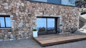 A modern house with a stone facade, large sliding glass doors, and a wooden deck with outdoor seating. - Apartment (Viggianello)