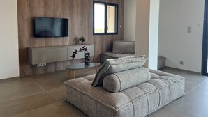 A modern living room with a grey sofa, a small round table, a mounted TV, and a window with a view. - Apartment (Viggianello)