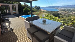Une terrasse extérieure avec une table et des chaises, une piscine et une vue panoramique sur un paysage côtier.