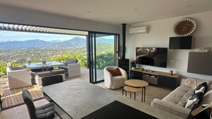 Un salon moderne doté d’un grand téléviseur, de sièges confortables et offrant une vue sur un paysage montagneux.
