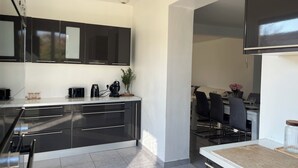 A modern kitchen with black cabinets, a countertop, and a dining area with chairs and a table. - Villa with pool and air conditioning (Carpentras)