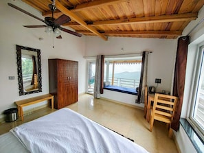 A bedroom with a bed, a wardrobe, a ceiling fan, a window with curtains, and a view of the outdoors.