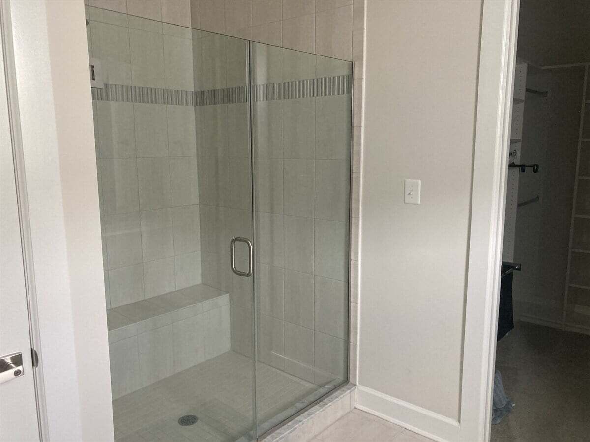 Une douche fermée par des parois de verre, avec un sol carrelé et une porte.