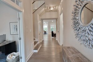 A hallway with a staircase, a dog bed, a mirror, and a framed picture on the wall.