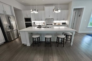 A modern kitchen with white cabinetry, a large island with stools, stainless steel appliances, and pendant lighting.