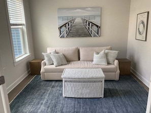 A living room with a sofa, two pillows, a side table, a framed picture, and a blue rug.