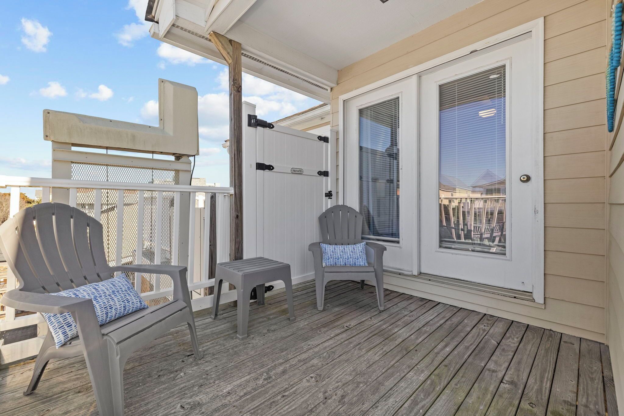 A covered deck with two Adirondack chairs, a small table, and a sliding glass door.