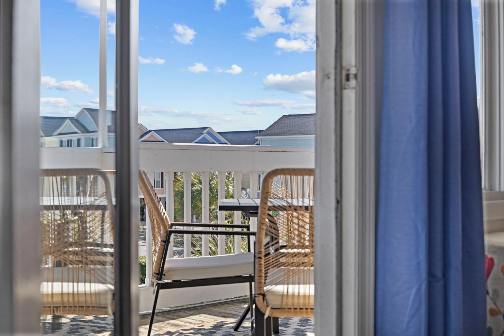 Een balkon met rieten stoelen en een tafel, met uitzicht op een woonwijk met huizen en een heldere lucht.