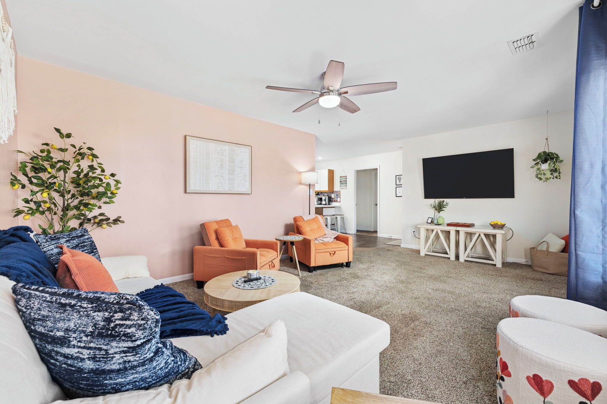 Een moderne woonkamer met een witte bank, oranje fauteuils, een plafondventilator, een televisie en een kleine tafel met een plant.