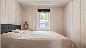 Un dormitorio con cama, ventana y paredes de madera.