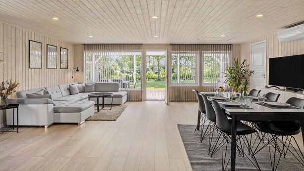 Una sala de estar moderna con un sofá modular, un comedor con mesa y sillas, y ventanas amplias que ofrecen vistas al exterior.