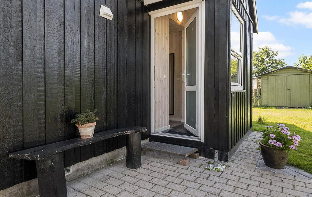 Un edificio de madera con fachada oscura, un banco y una puerta de entrada.