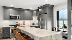 Una cocina moderna con armarios grises, electrodomésticos de acero inoxidable, una isla de mármol y un amplio ventanal.