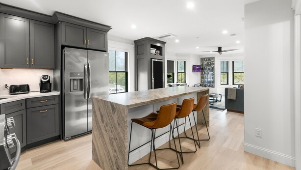 Una cocina moderna con una isla grande, taburetes de bar y un refrigerador empotrado.