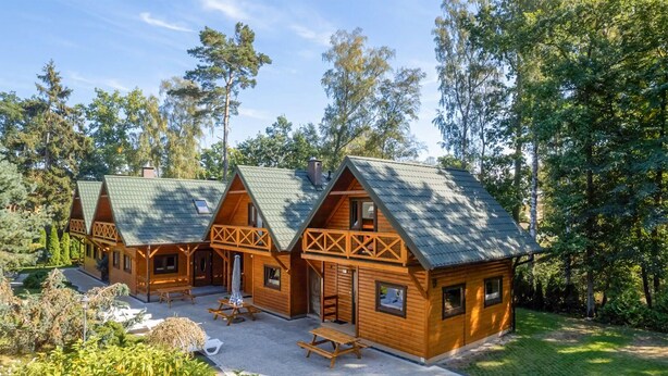 Een rij houten chalets met schuine daken, een centrale ingang en een picknicktafel op de voorgrond.