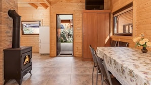 Een knus houten vakantiehuisje met een open haard, een televisie en een eethoek met een tafel en stoelen.