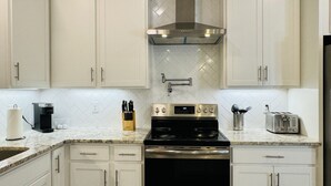 Una cocina con gabinetes blancos, una campana extractora de acero inoxidable, una estufa negra y un tostador.