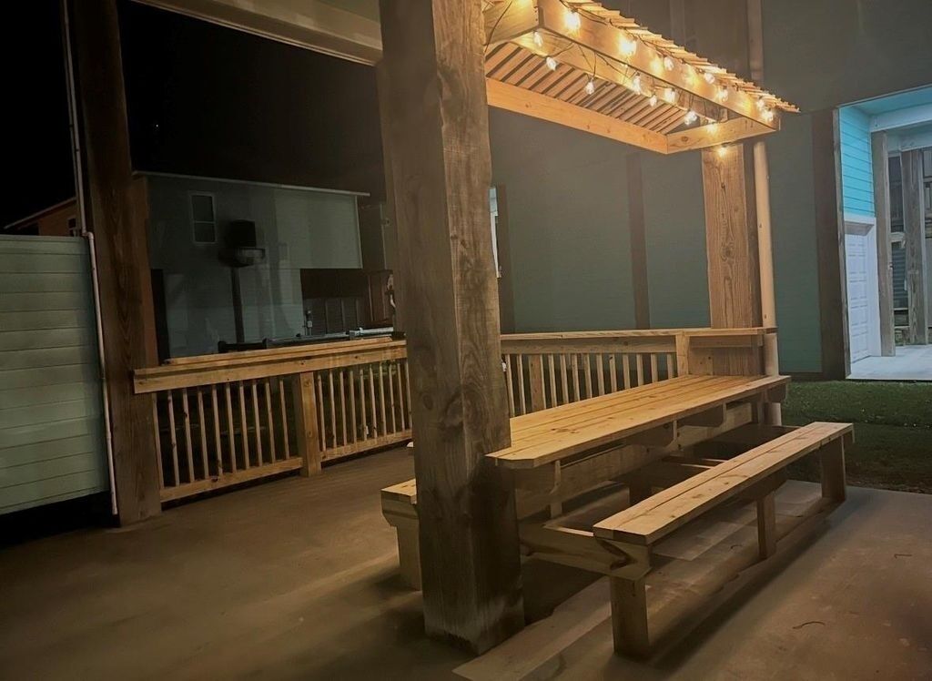 An outdoor wooden deck with benches and a pergola with lights.