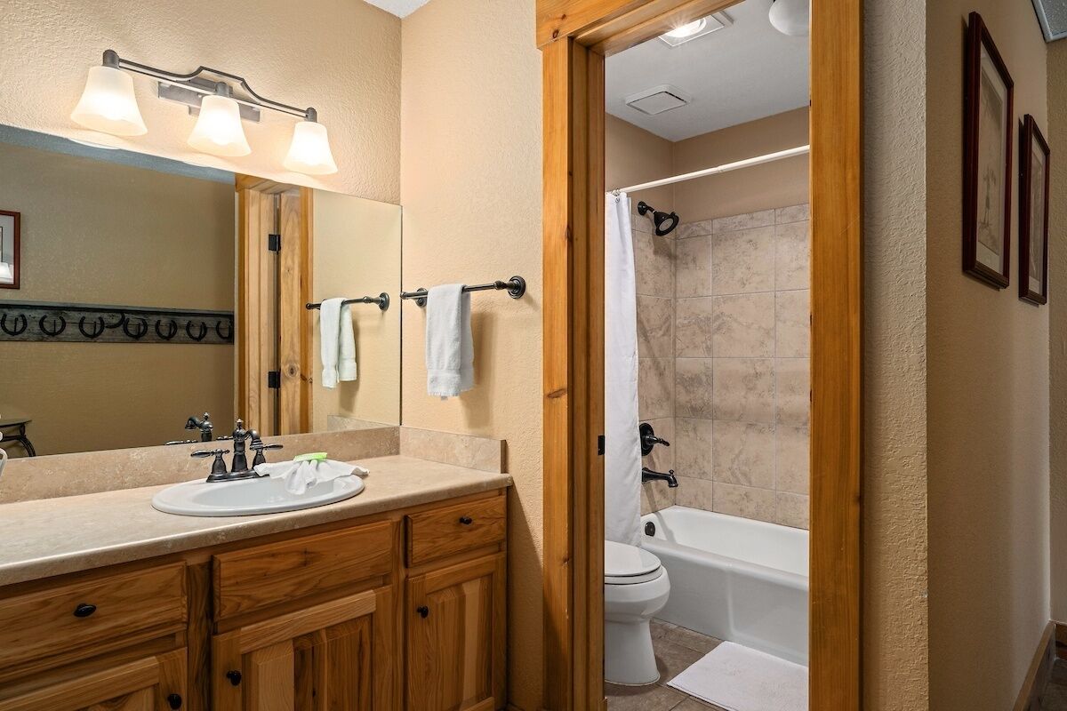 A bathroom with a wooden vanity, a sink, a mirror, and a shower area.
