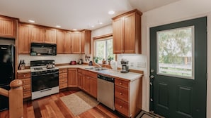 A modern kitchen with wooden cabinets, a black refrigerator, a stove, and a dishwasher. - 77mbr - Wi-fi - Fireplace - Pets Ok - Bbq 3 Bedroom Cabin by RedAwning (Deming)