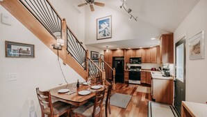 A modern kitchen with wooden cabinets, a dining area with a wooden table and chairs, and a staircase with a wooden railing. - 77mbr - Wi-fi - Fireplace - Pets Ok - Bbq 3 Bedroom Cabin by RedAwning (Deming)
