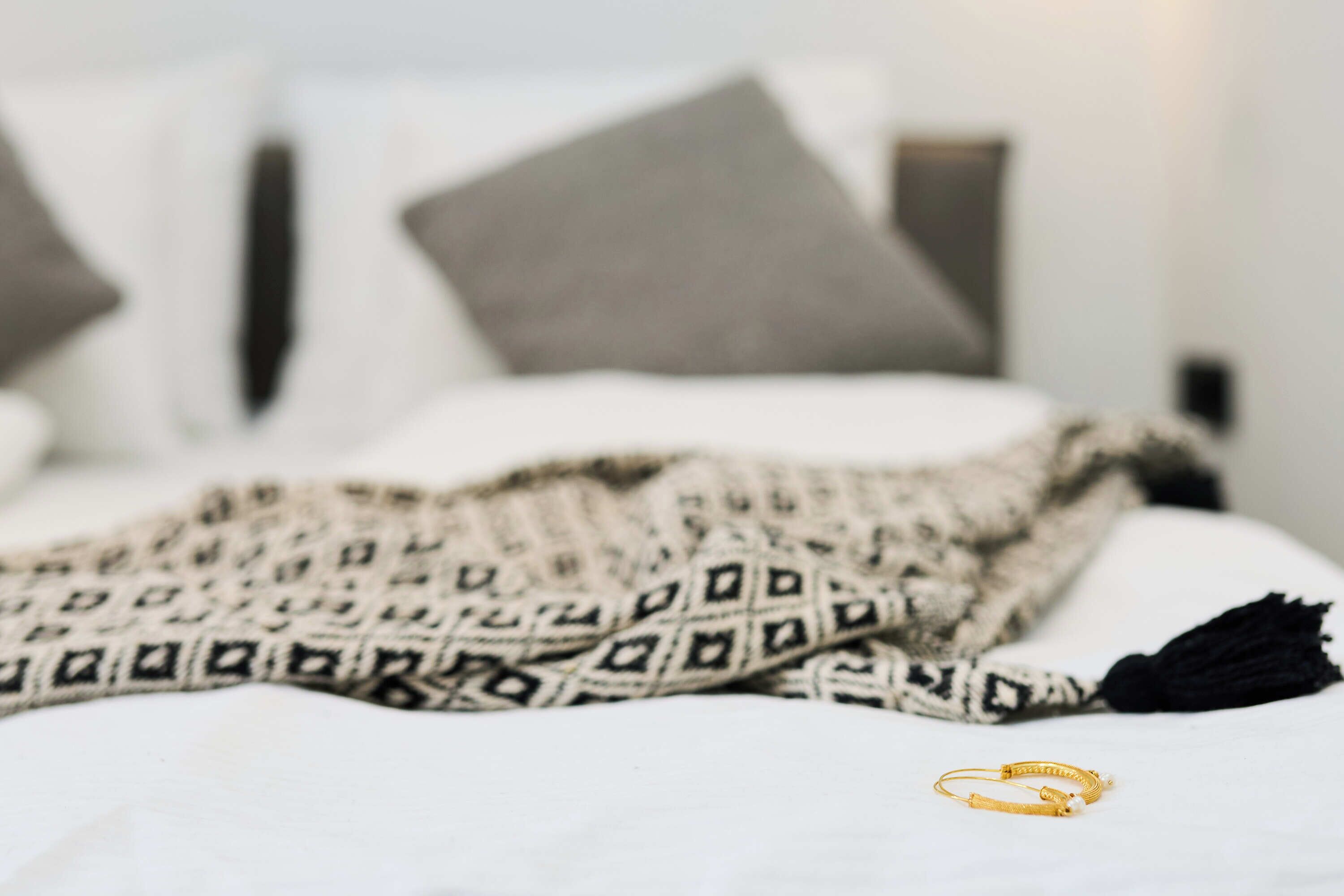 A bed with a patterned blanket and a black tassel, a gold bracelet, and a pillow.