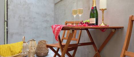 A wooden table with a bottle of champagne, two glasses, and a candle. There are wicker baskets and a red and white checkered cloth on the table.