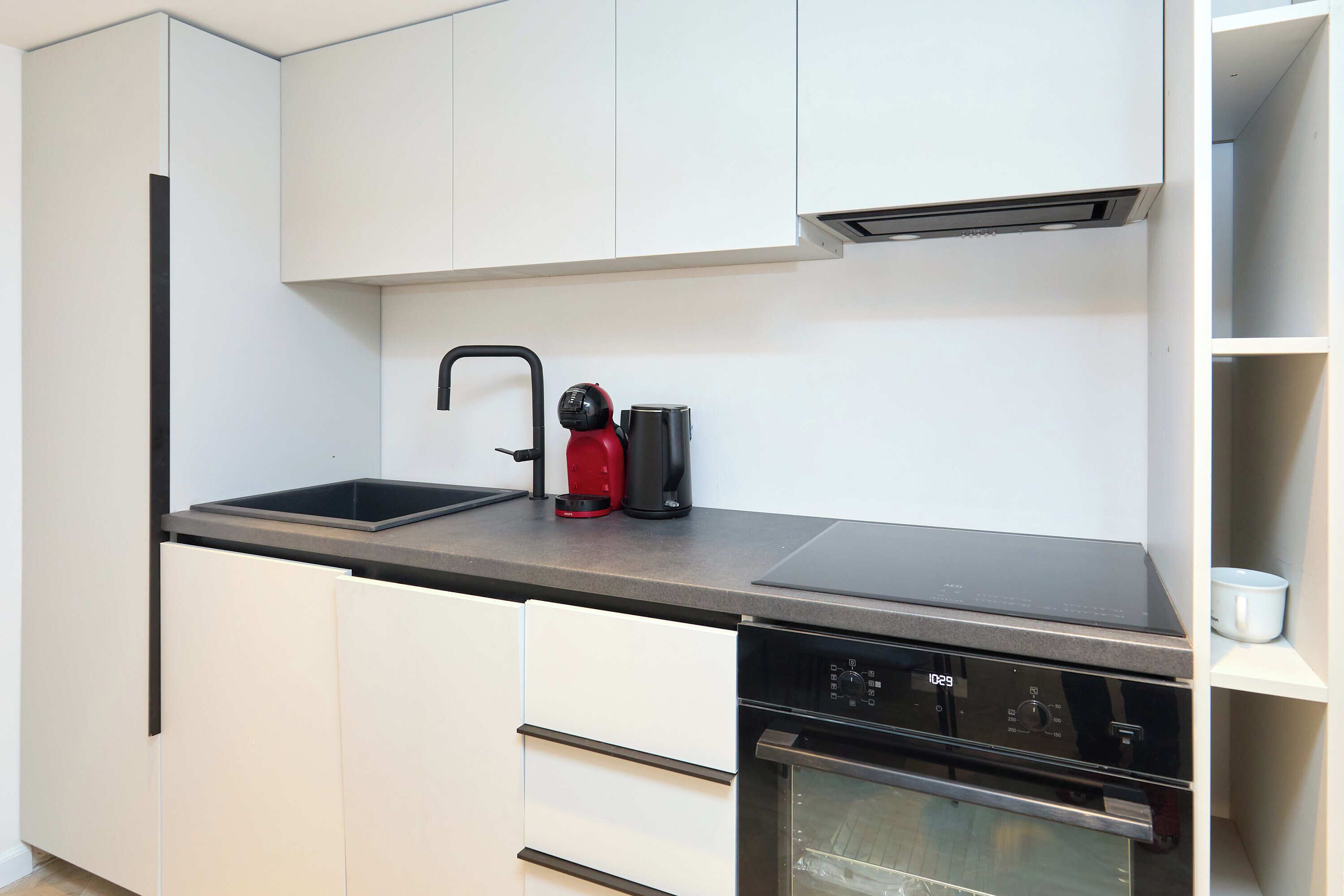 A modern kitchen with white cabinets, a black countertop, a coffee maker, and a dishwasher.