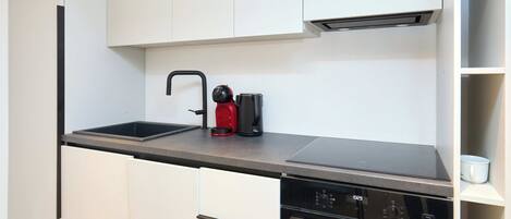 A modern kitchen with white cabinets, a black countertop, a coffee maker, and a dishwasher.