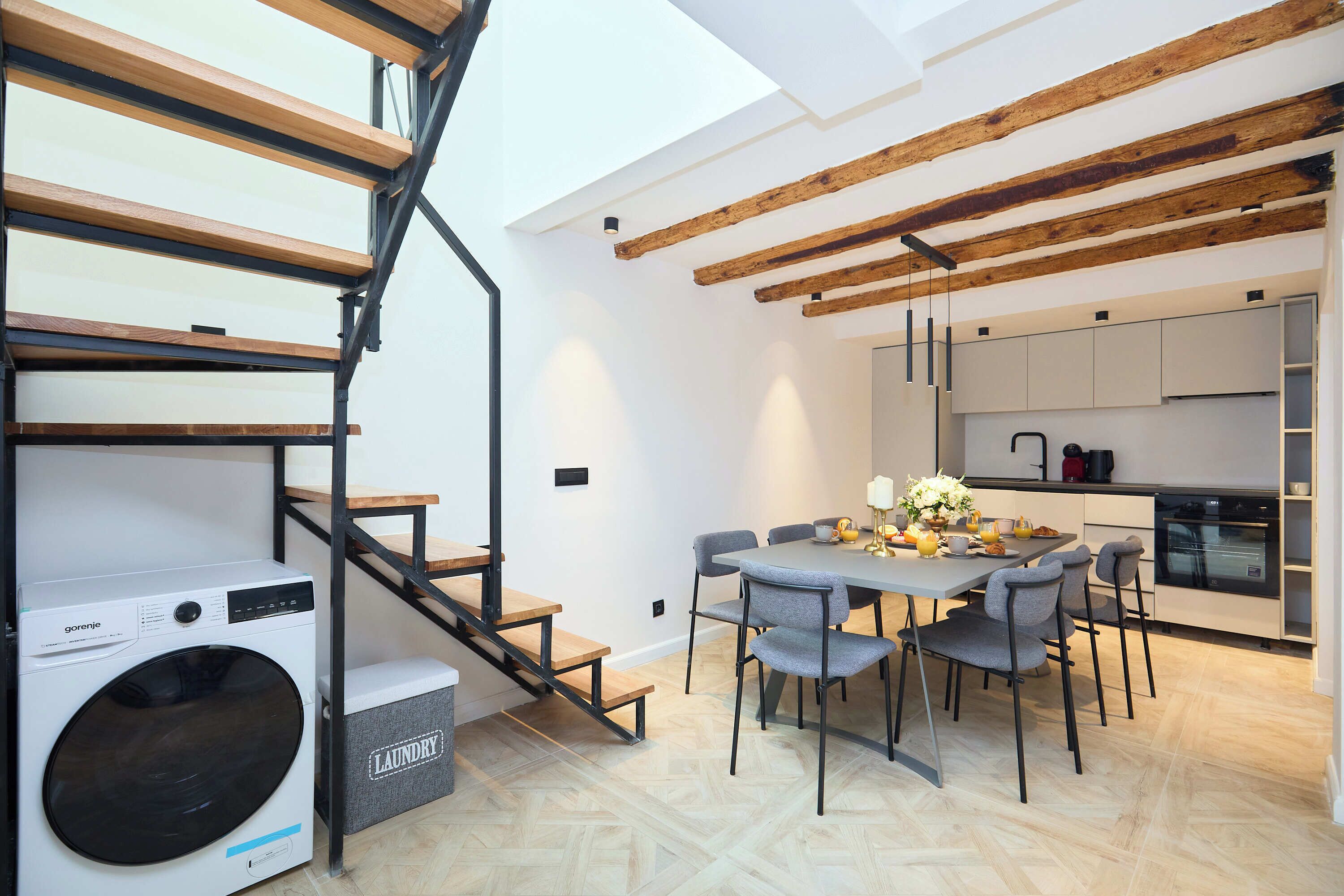 A modern kitchen with white cabinets, a built-in oven, and a dining area with grey chairs and a table.