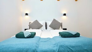 A neatly made bed with two pillows, a blue blanket, and two folded towels. There are two wall-mounted light fixtures on either side of the bed. - Black Water Bay house (Dubrovnik)