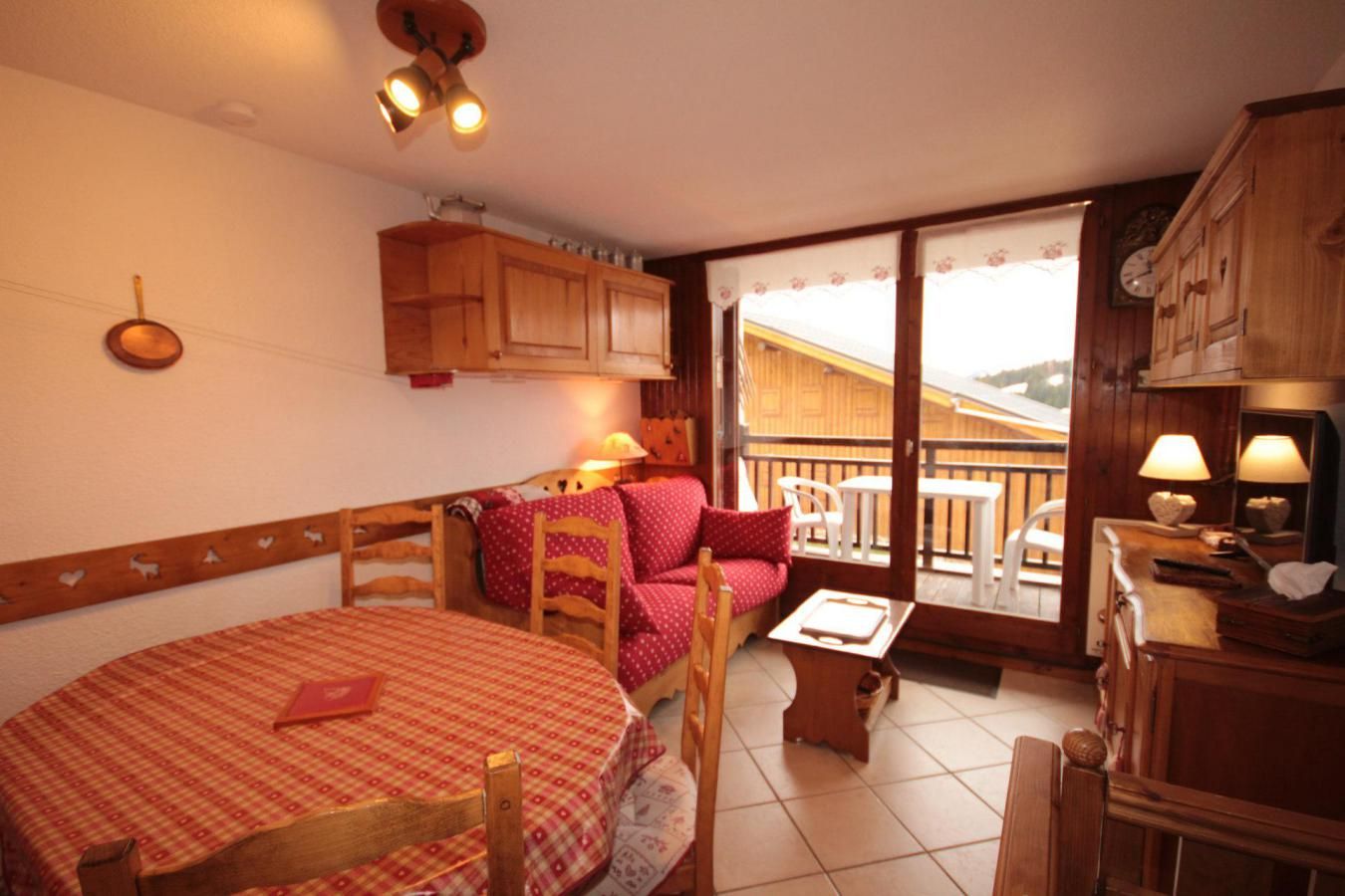 Una habitación acogedora con una mesa y sillas de madera, un pequeño sofá, un balcón con vistas y armarios de madera.
