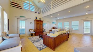 A spacious living room with a high ceiling, a large wooden cabinet, a sofa, and a dining area with a table and chairs.