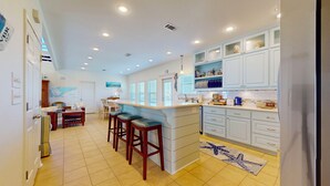 A kitchen with white cabinets, a central island, bar stools, and a tiled floor.