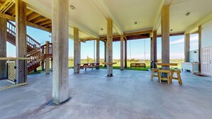 A covered outdoor area with wooden beams, picnic tables, a swing, and a view of the landscape.