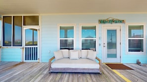 A room with a wooden floor, a white sofa with cushions, a wooden bench, and a door labeled 'BEACHY KEN'.