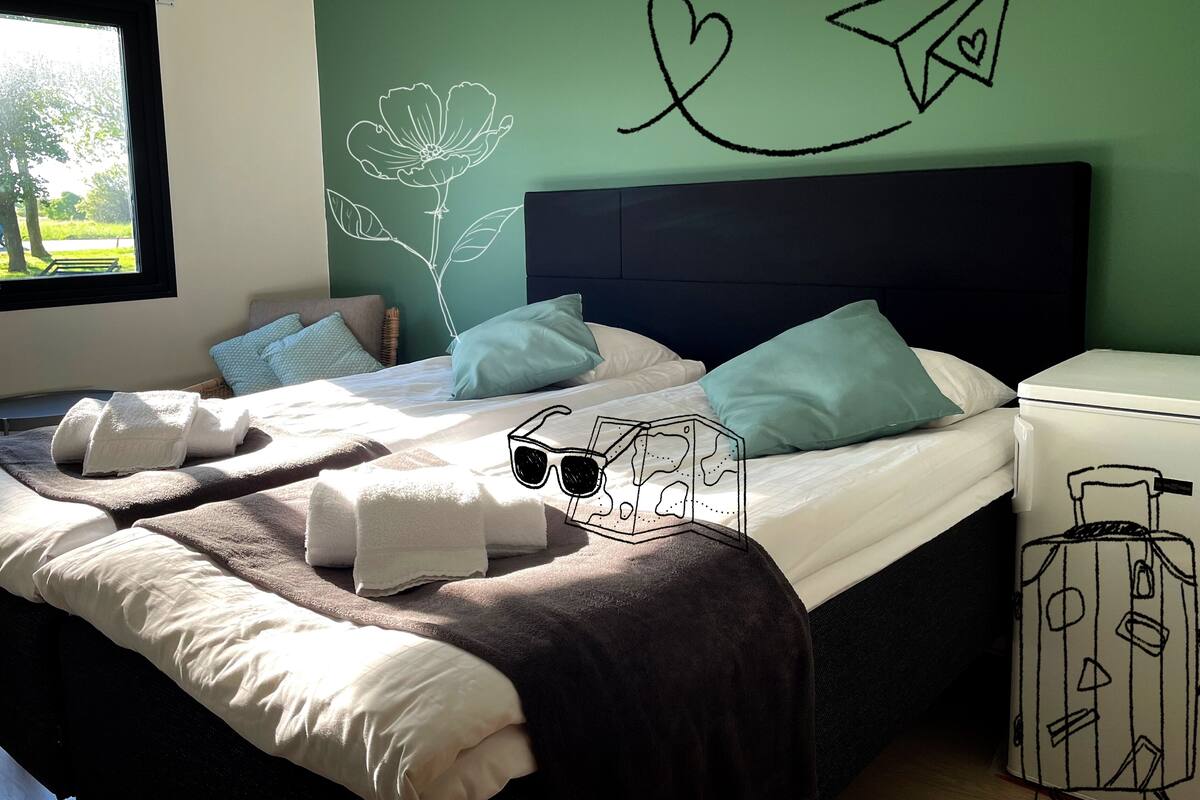 A bedroom with a bed, pillows, a headboard, and a wall with a flower and paper airplane drawing.